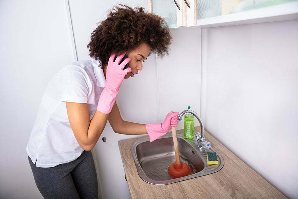 Woman plunging her blocked sink while on the phone