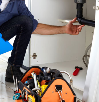 Plumber with bag of tools working on pipe under sink