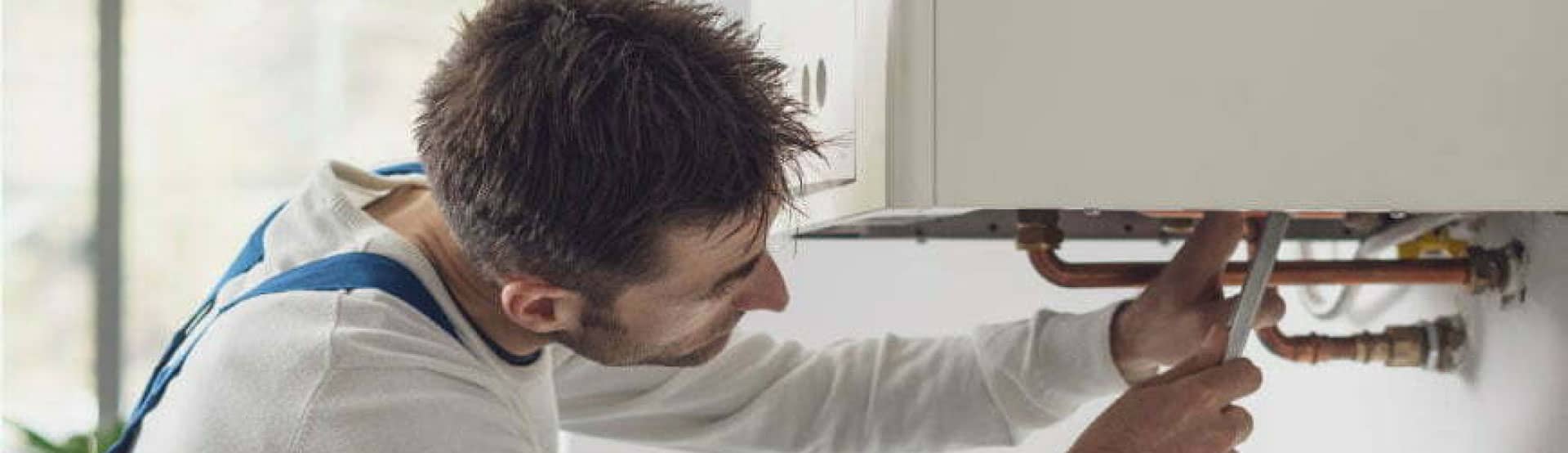 Plumber reaching into the bottom of a hot water system with tools